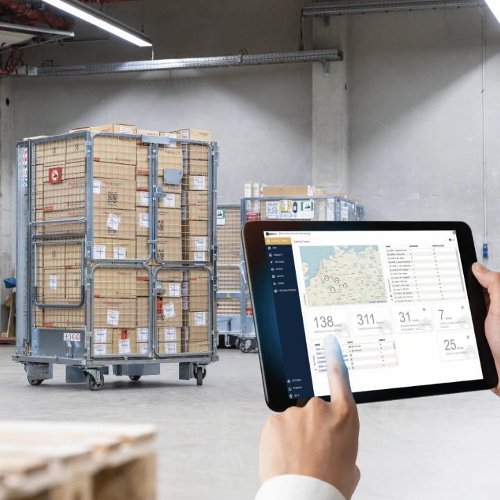 Warehouse employee in safety vest uses tablet to manage load carriers.